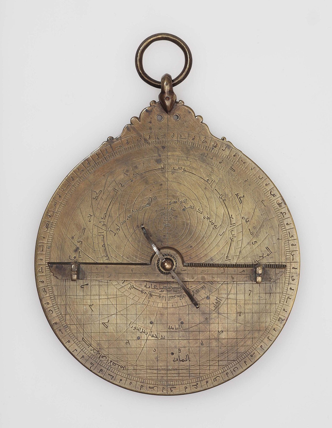 The back of an intricate brass astrolabe, a historical astronomical instrument used for navigation and timekeeping, covered in engraved scales and markings.